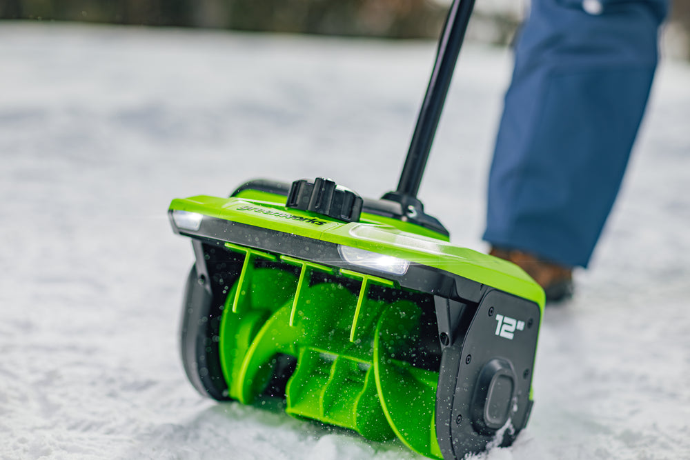 Green snow shovel being used to clear snow on a driveway