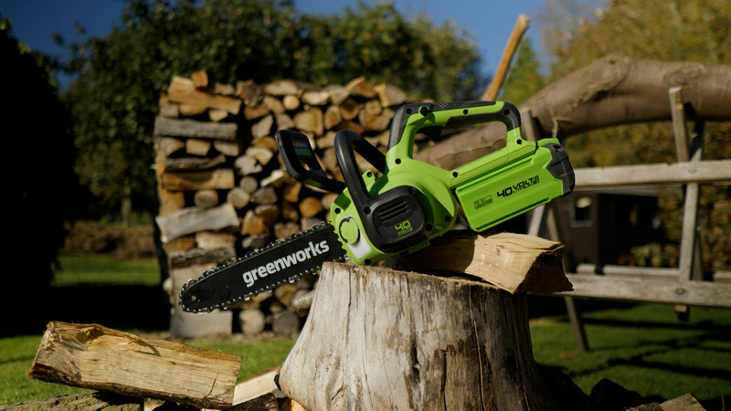 Greenworks chainsaw on a log with stacked firewood in the background