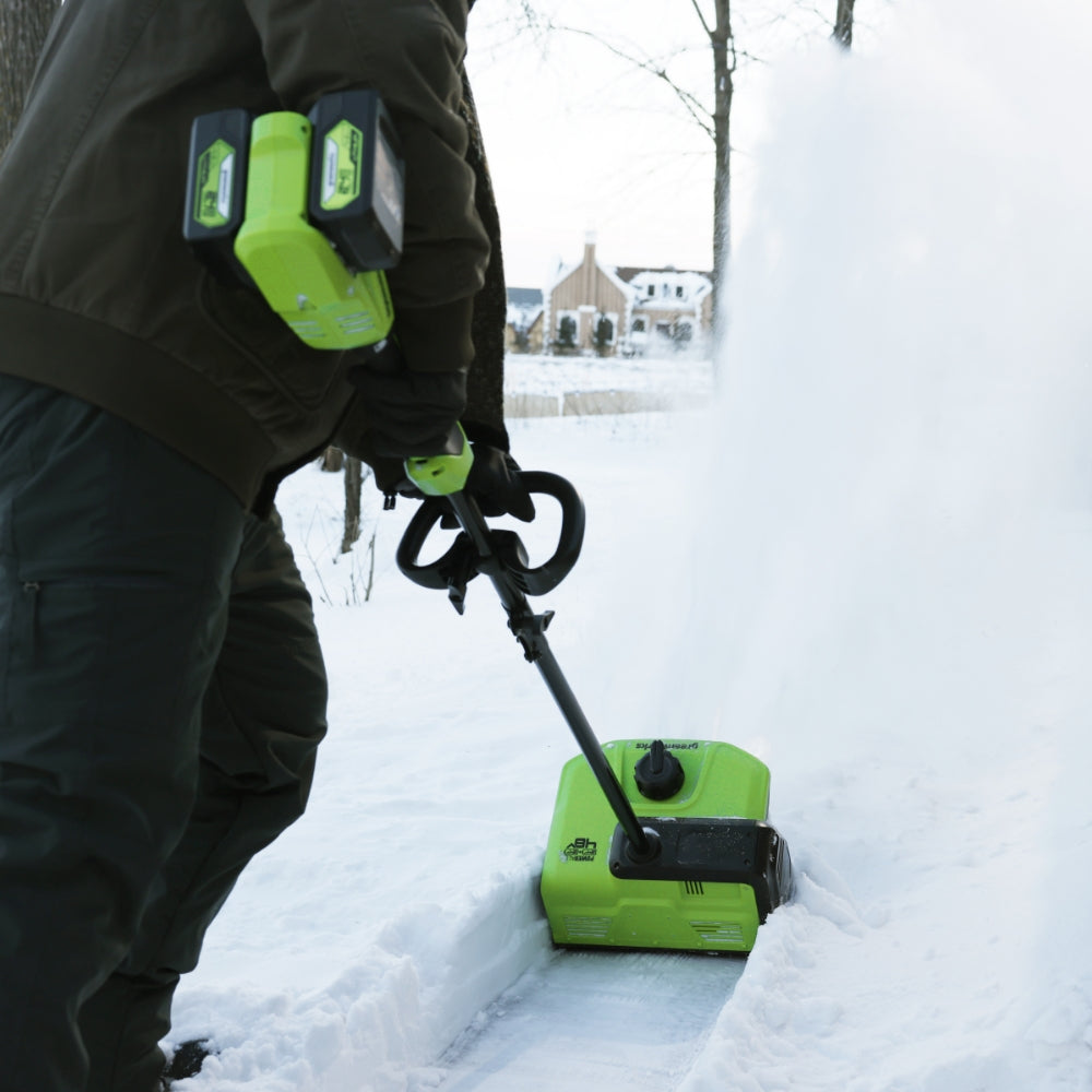 Person using a green snow blower in a snowy outdoor setting