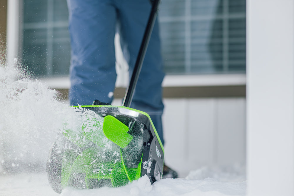 Person using a green and black snow shovel to clear snow
