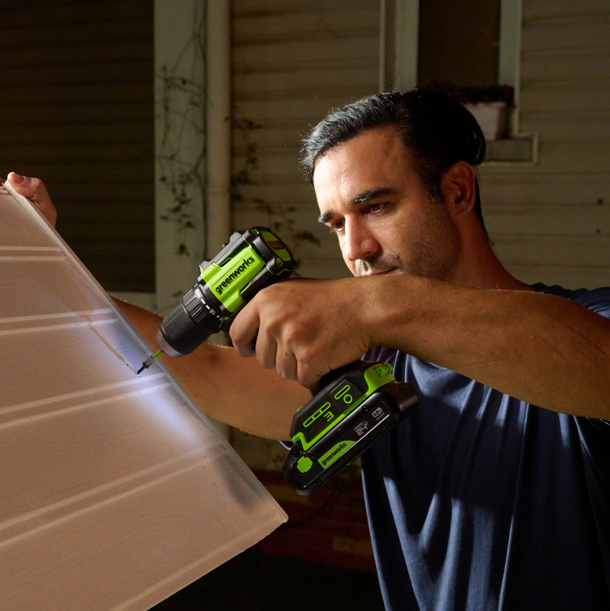 Man using a green and black power drill on a wooden surface