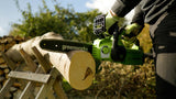 Person using a Greenworks chainsaw to cut a log outdoors.