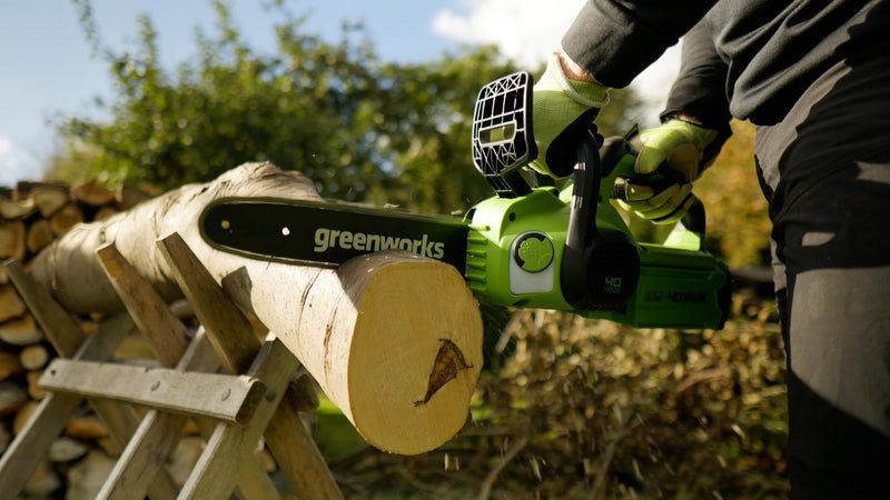 Person using a Greenworks chainsaw to cut a log outdoors.