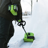 Person using a green snow blower in a snowy outdoor setting
