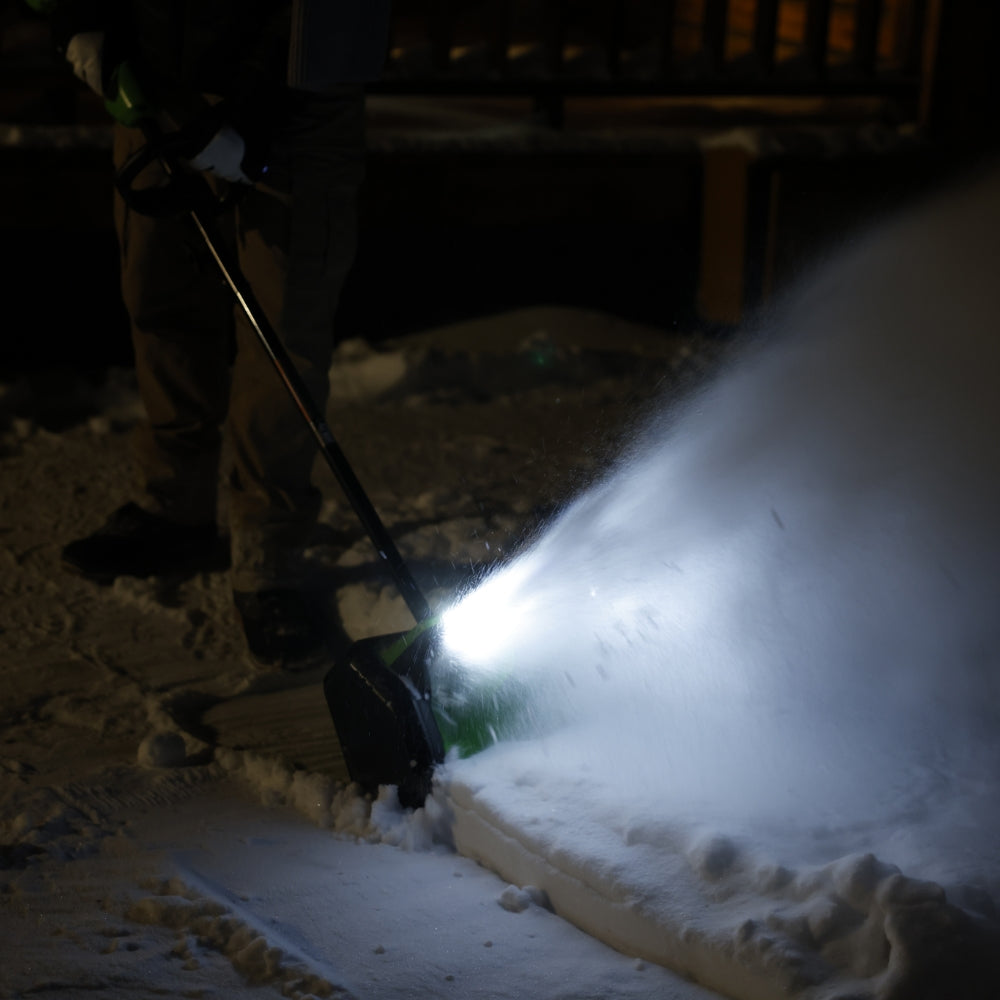 Person using a snow blower to clear snow at night.